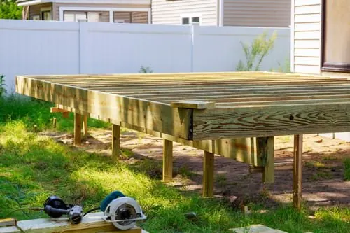 Elevated residential wood deck with railing and support posts in a back yard